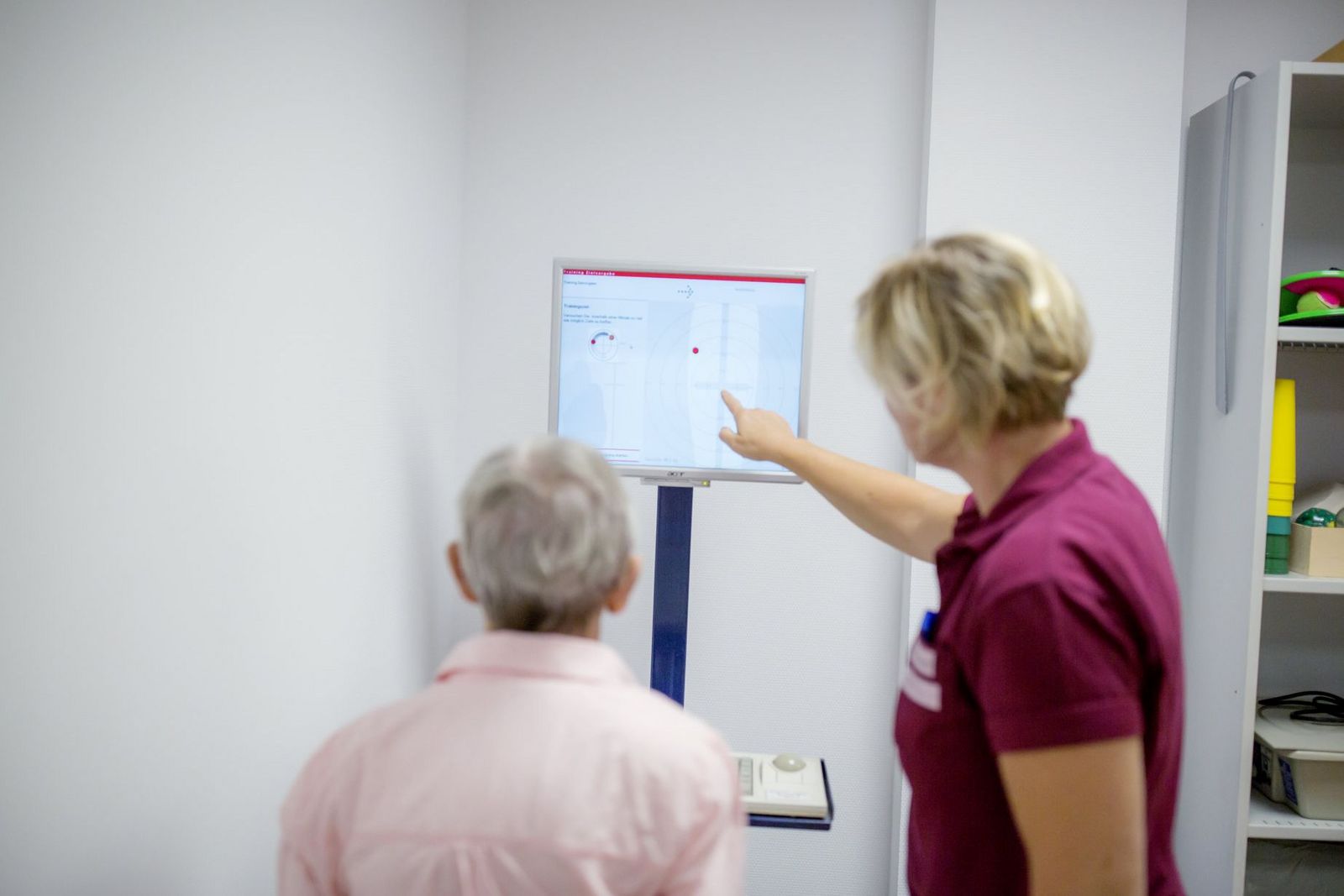 eine Ergotherapeutin zeigt einer Patientin etwas auf dem Bildschirm